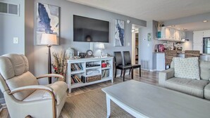 Ein Wohnzimmer mit einer Couch, Sesseln, einem Couchtisch, einem Fernseher und einem Bücherregal.