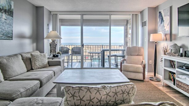 Ein Wohnzimmer mit einer Couch, einem Sessel und einem Couchtisch. Ein Balkon bietet Blick auf das Meer.