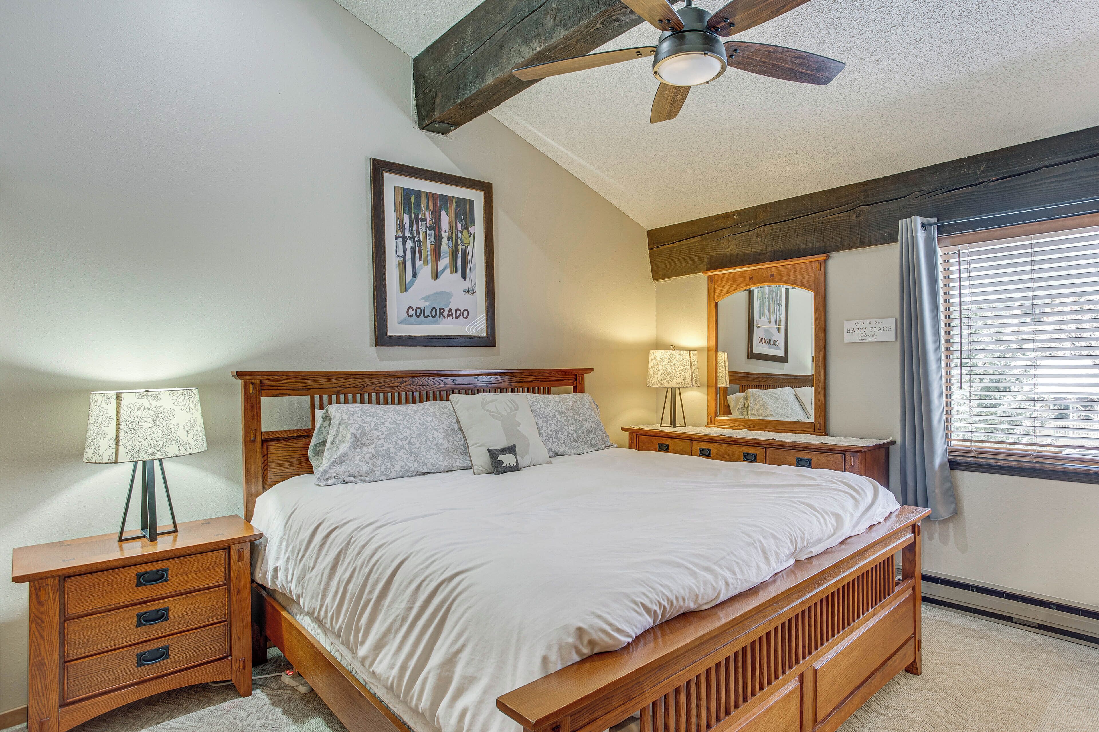 A bedroom with a wooden bed, nightstands, a ceiling fan, a window with blinds, and a framed picture on the wall.