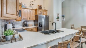 A modern kitchen with wooden cabinets, a stainless steel refrigerator, a large island with a sink, and rustic wooden chairs. - Colorado Escape w/ Pool Access & Mountain Views! (Avon)