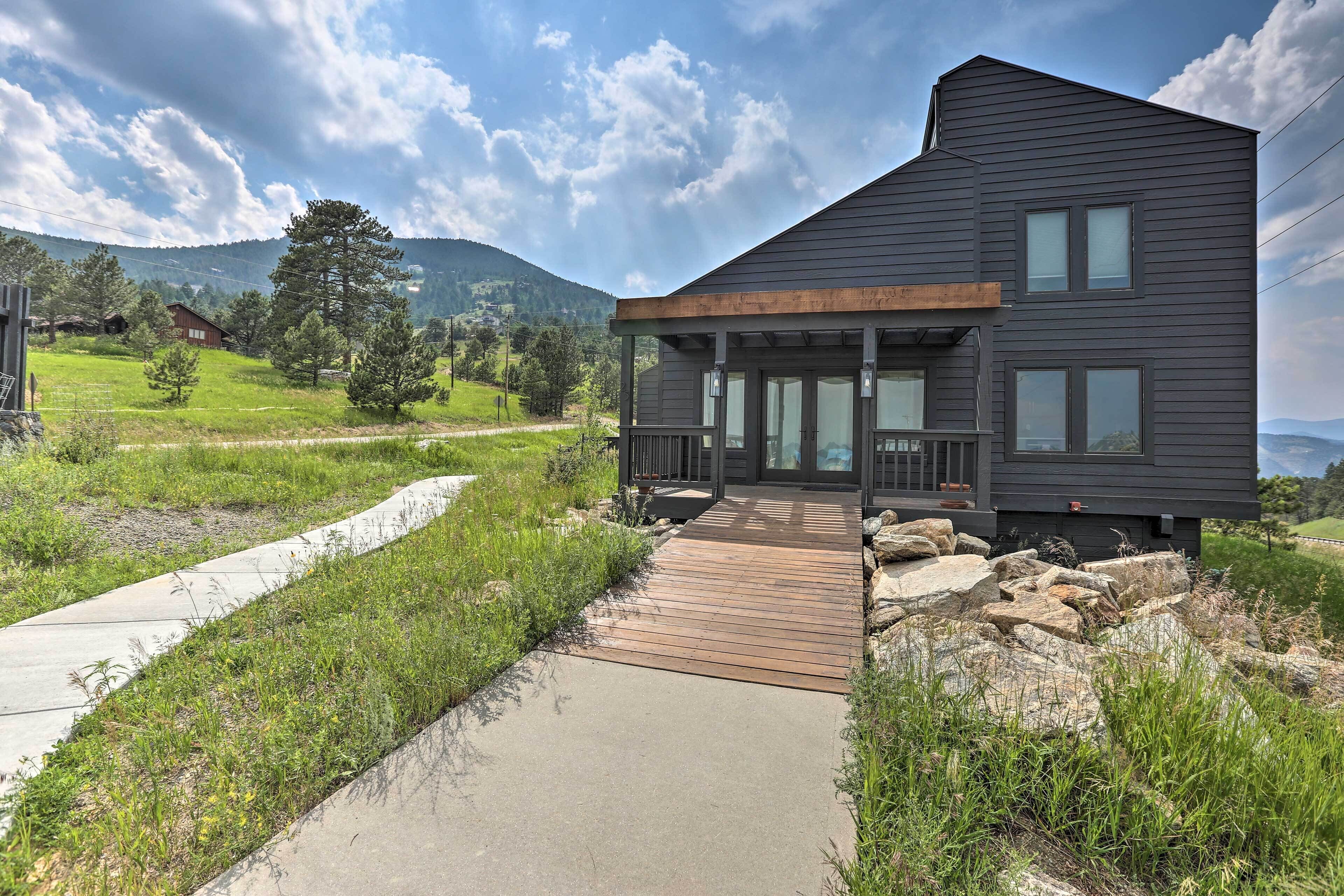Une maison moderne dotée d’une terrasse en bois et d’un chemin en béton menant à l’entrée.