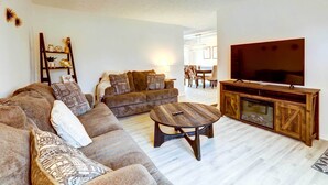 Una sala de estar con un sofá, una mesa de centro, un televisor sobre un mueble de madera y un comedor al fondo.