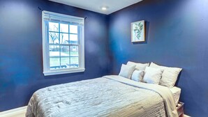 Un dormitorio con cama, ventana y un cuadro colgado en la pared.