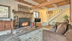 A cozy living room with a brick fireplace, wooden beams, a staircase, and a comfortable couch.