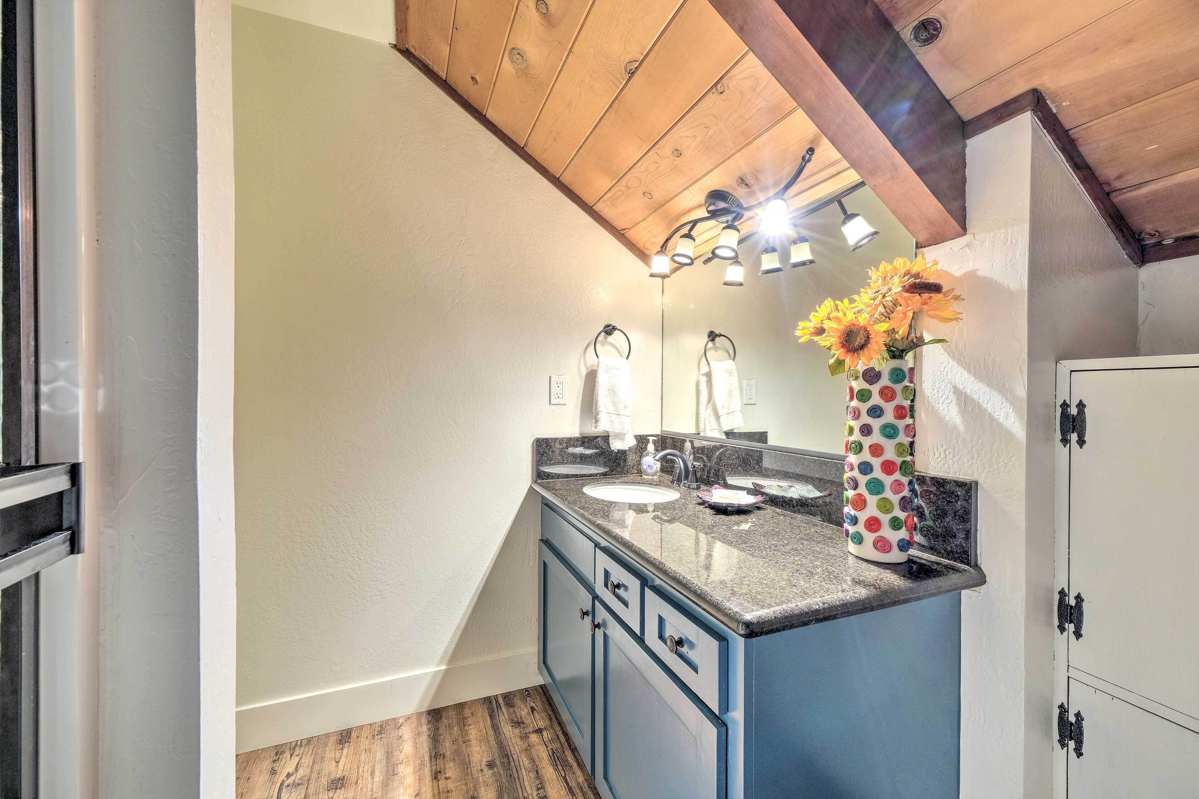 A bathroom with a wooden ceiling, a sink with a mirror, and a vase with sunflowers.