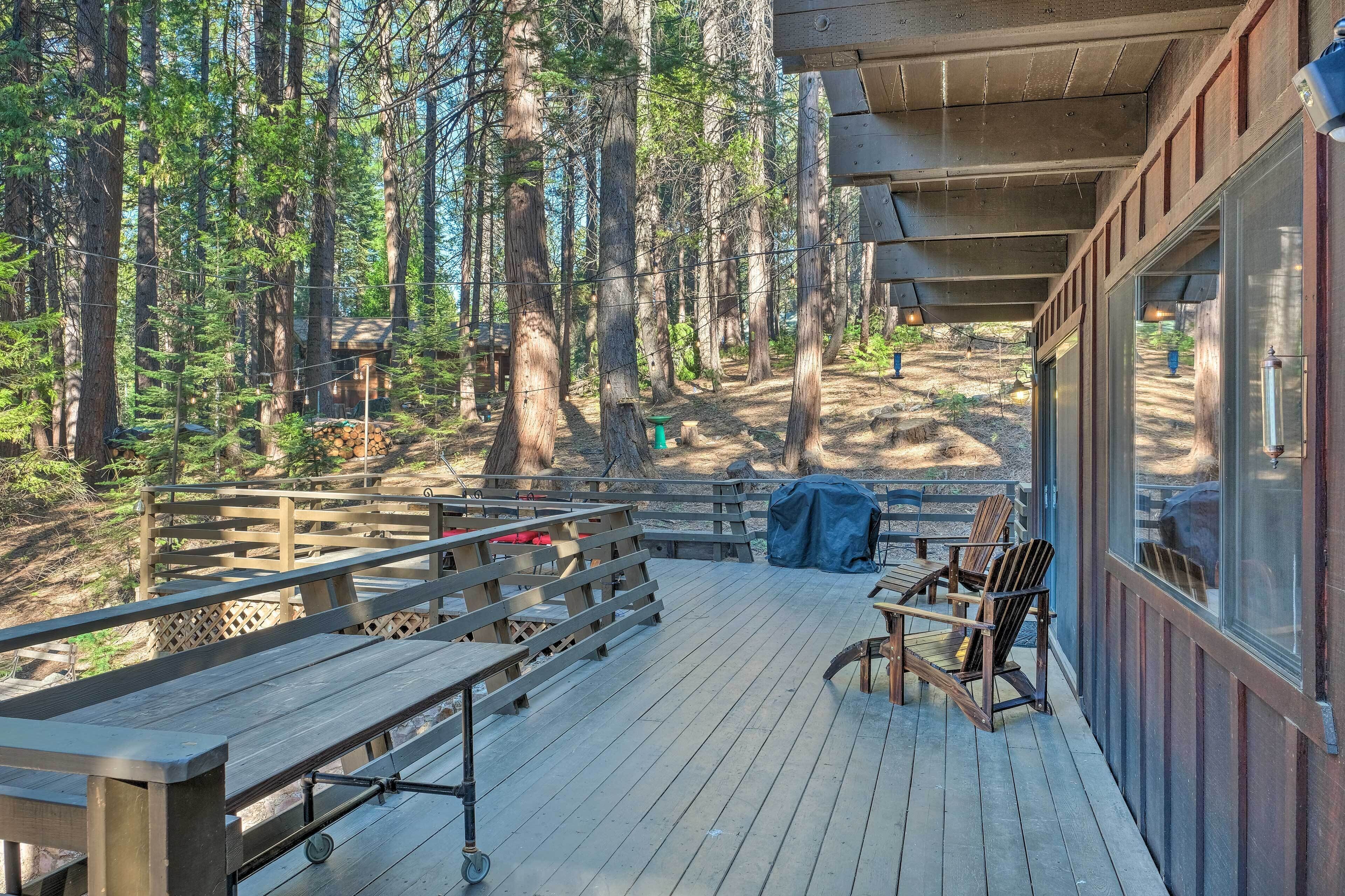 A wooden deck with benches and chairs, overlooking a forested area.