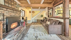A cozy living room with a fireplace, wooden beams, a staircase, and a sofa.