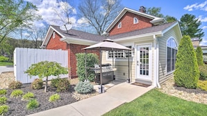 Una casa con patio coperto, barbecue e giardino recintato con diverse piante.