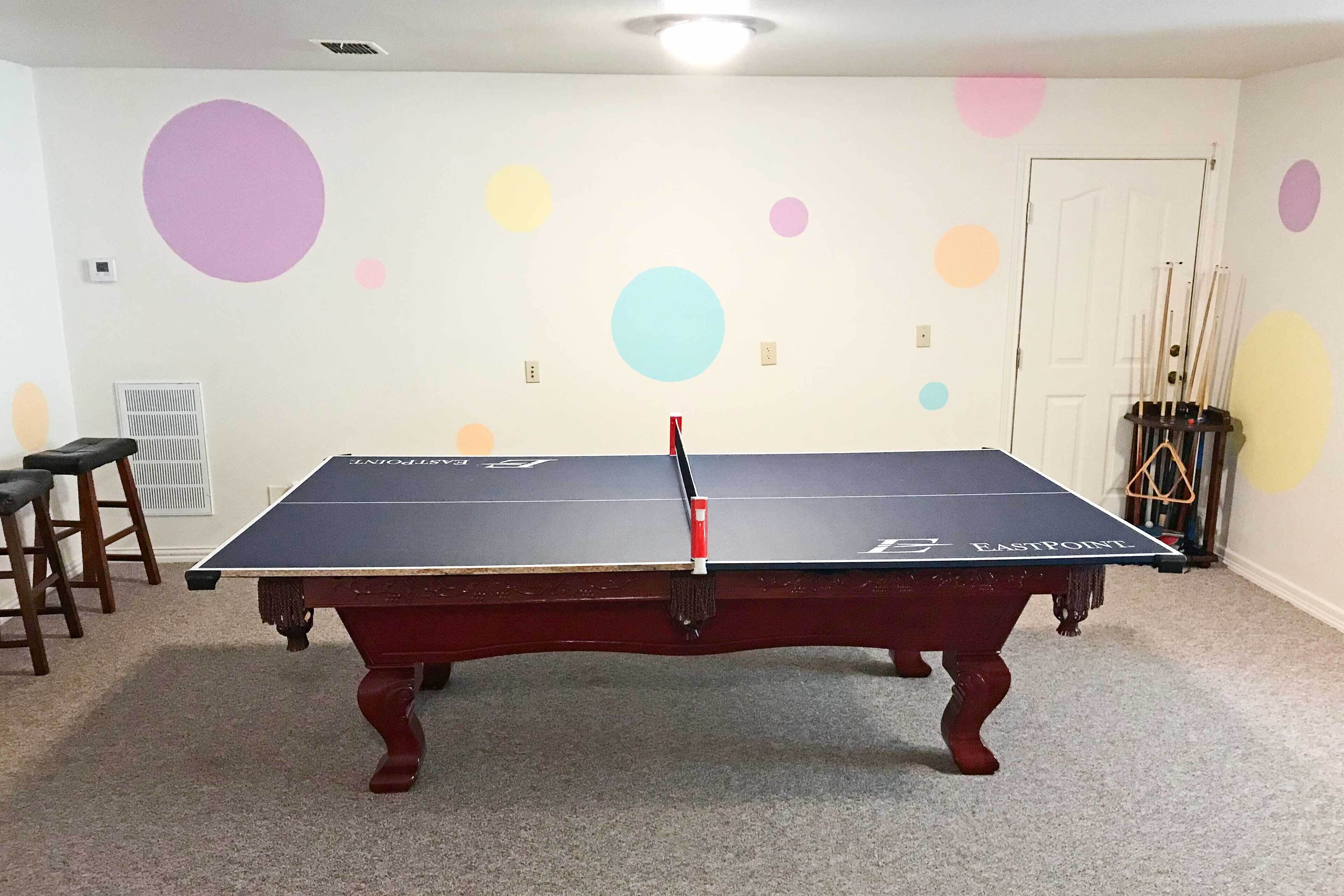 Une table de billard dans une pièce dont le mur blanc est décoré de cercles colorés.