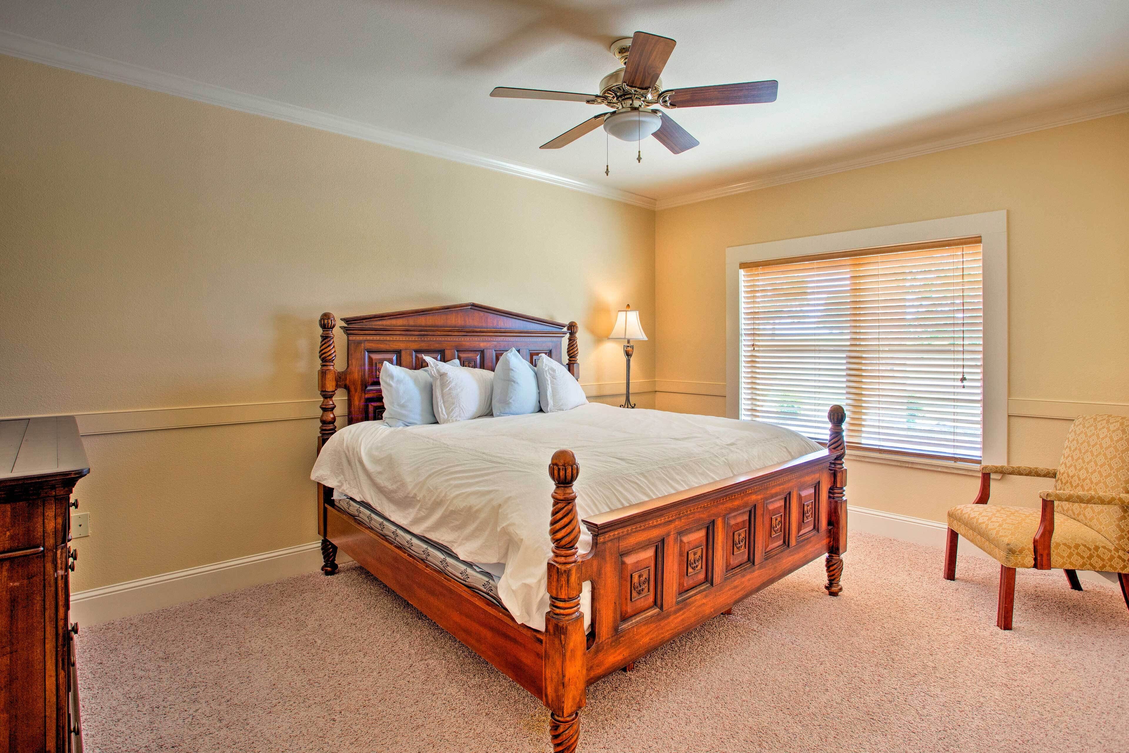 A bedroom with a wooden four-poster bed, a ceiling fan, a window with blinds, and a chair.