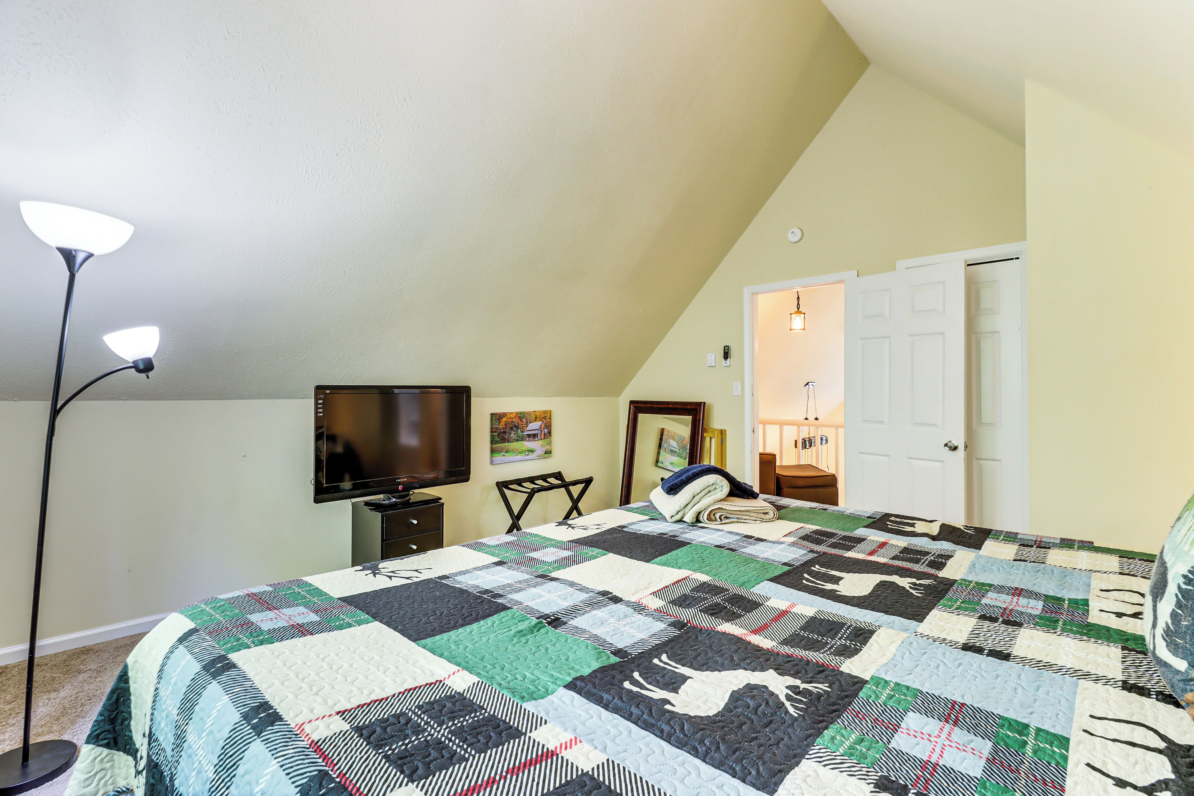 Ein Schlafzimmer mit einem großen Bett, einem Fernseher, einem Sessel und einer Tür zu einem weiteren Raum.