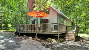 Eine Hütte mit einer Holzdielen-Terrasse, einer überdachten Sitzgelegenheit und einer Treppe zum Eingang.