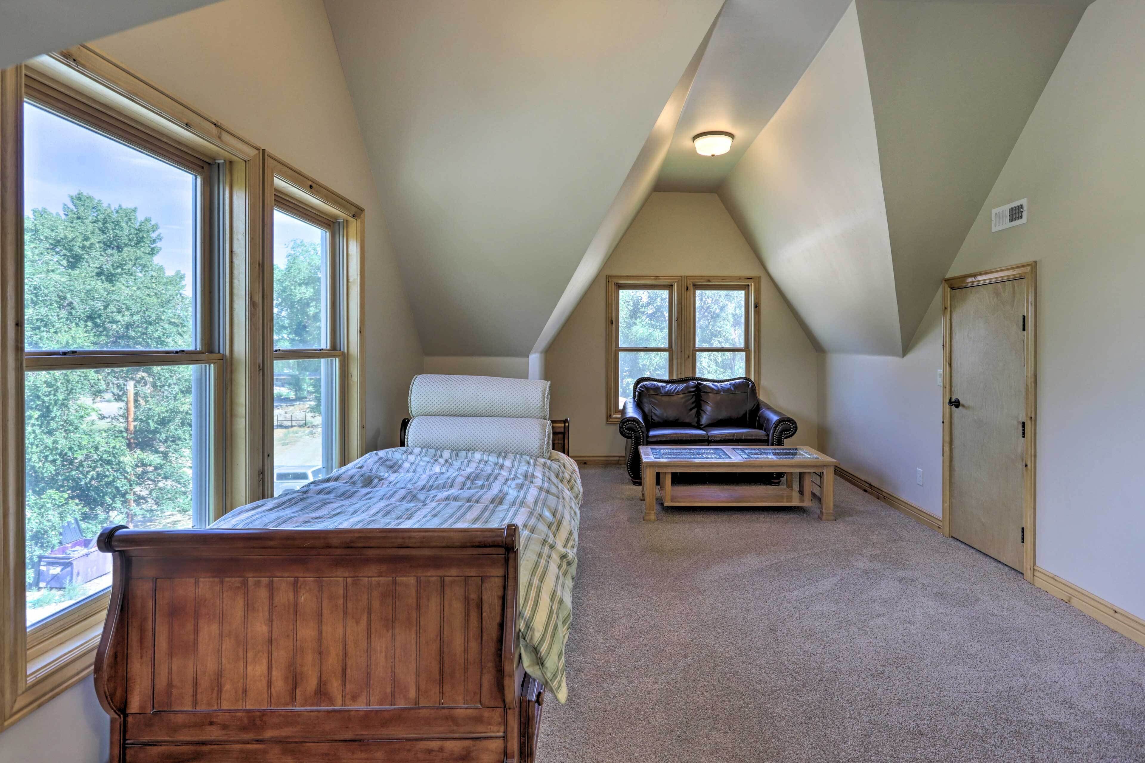 A bedroom with a large window, a bed, a chair, a table, and a door.