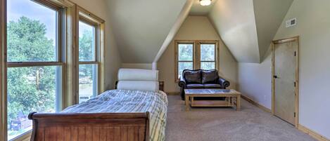 A bedroom with a large window, a bed, a chair, a table, and a door.