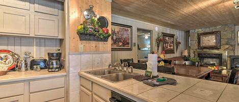 A kitchen with a wooden ceiling, a large island with a sink, and a stone fireplace.