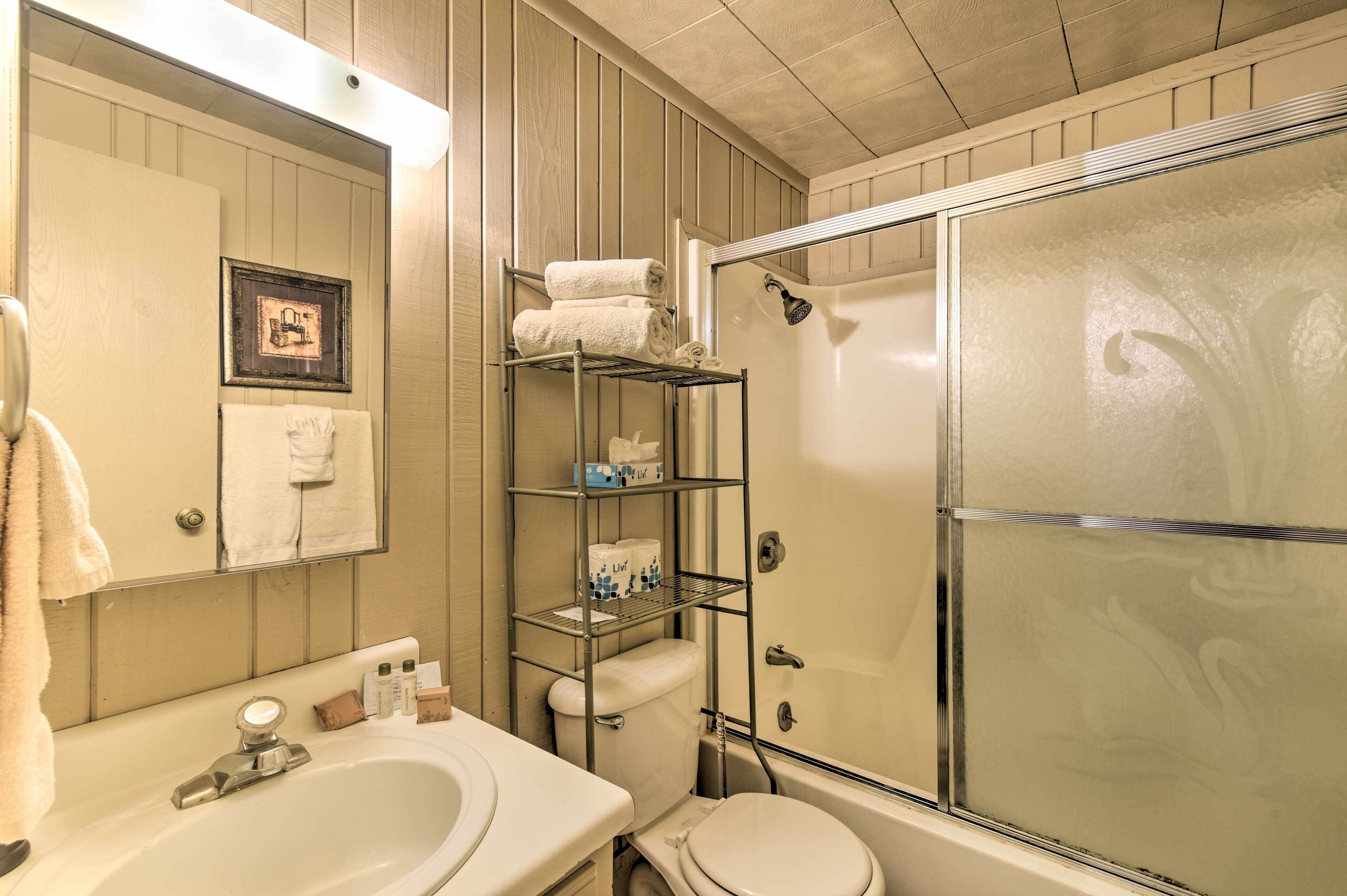 Une salle de bain équipée d’un lavabo, de toilettes et d’une douche à parois de verre. On y trouve des étagères avec des serviettes et des articles de toilette.