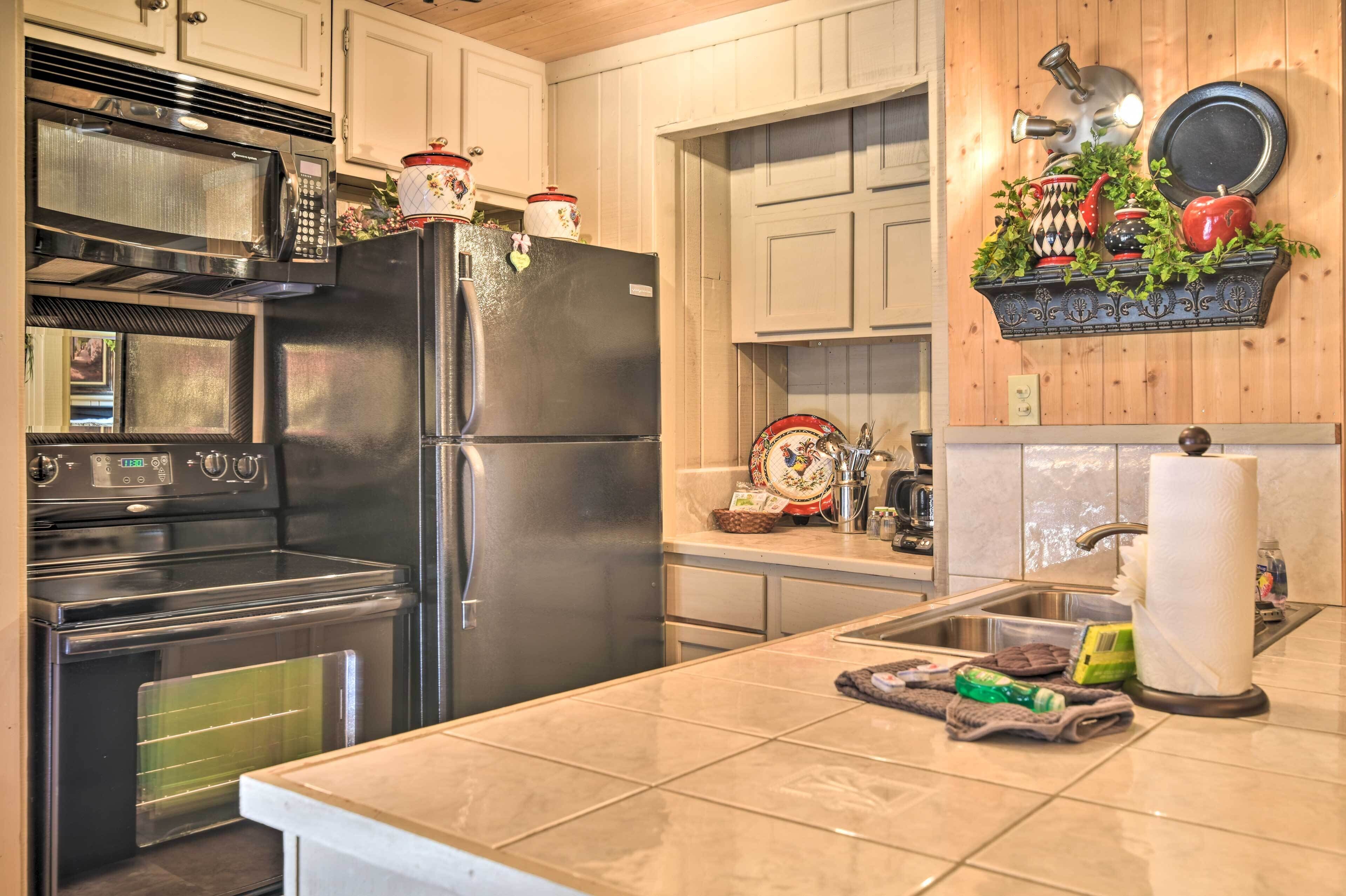 A kitchen with a stainless steel refrigerator, oven, and microwave. There is a wooden shelf with decorative items and a sink with a faucet.