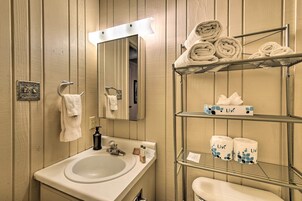 Un baño con lavamanos, espejo, toallero, repisas con toallas y papel higiénico.