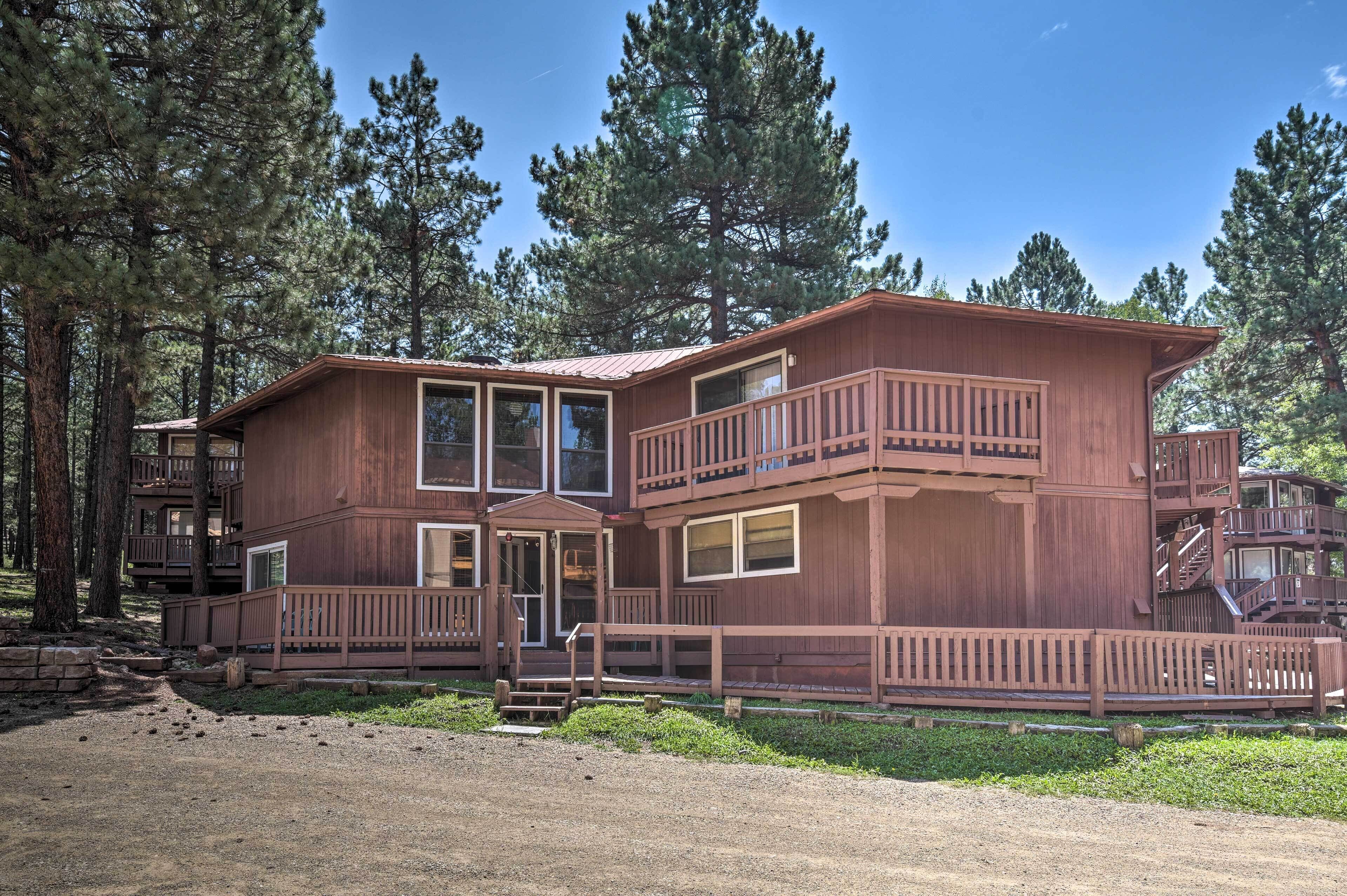 A two-story wooden cabin with a balcony, surrounded by tall pine trees.