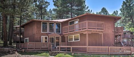 A two-story wooden cabin with a balcony, surrounded by tall pine trees.