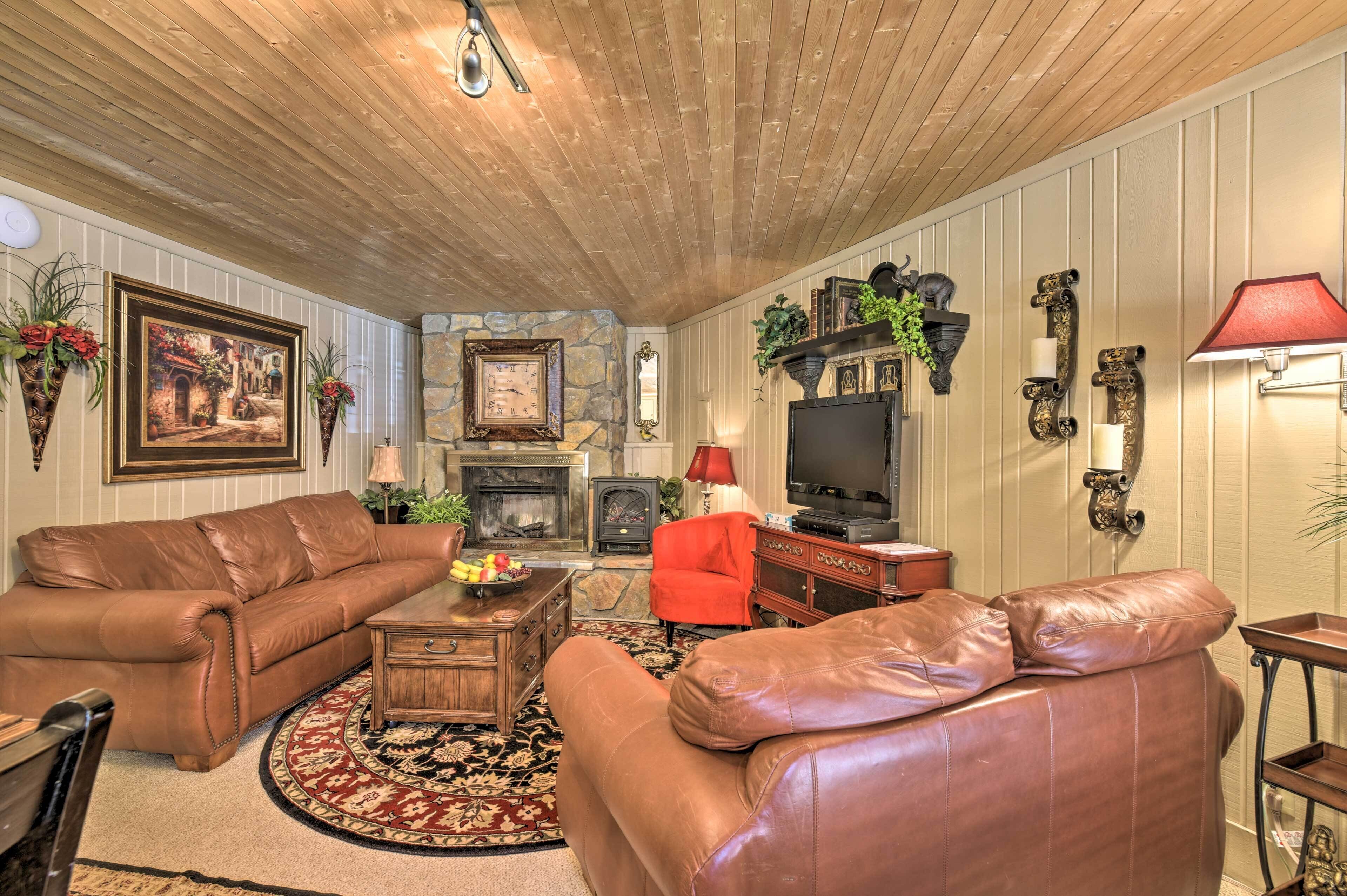 A living room with leather sofas, a fireplace, a television, and decorative wall sconces.