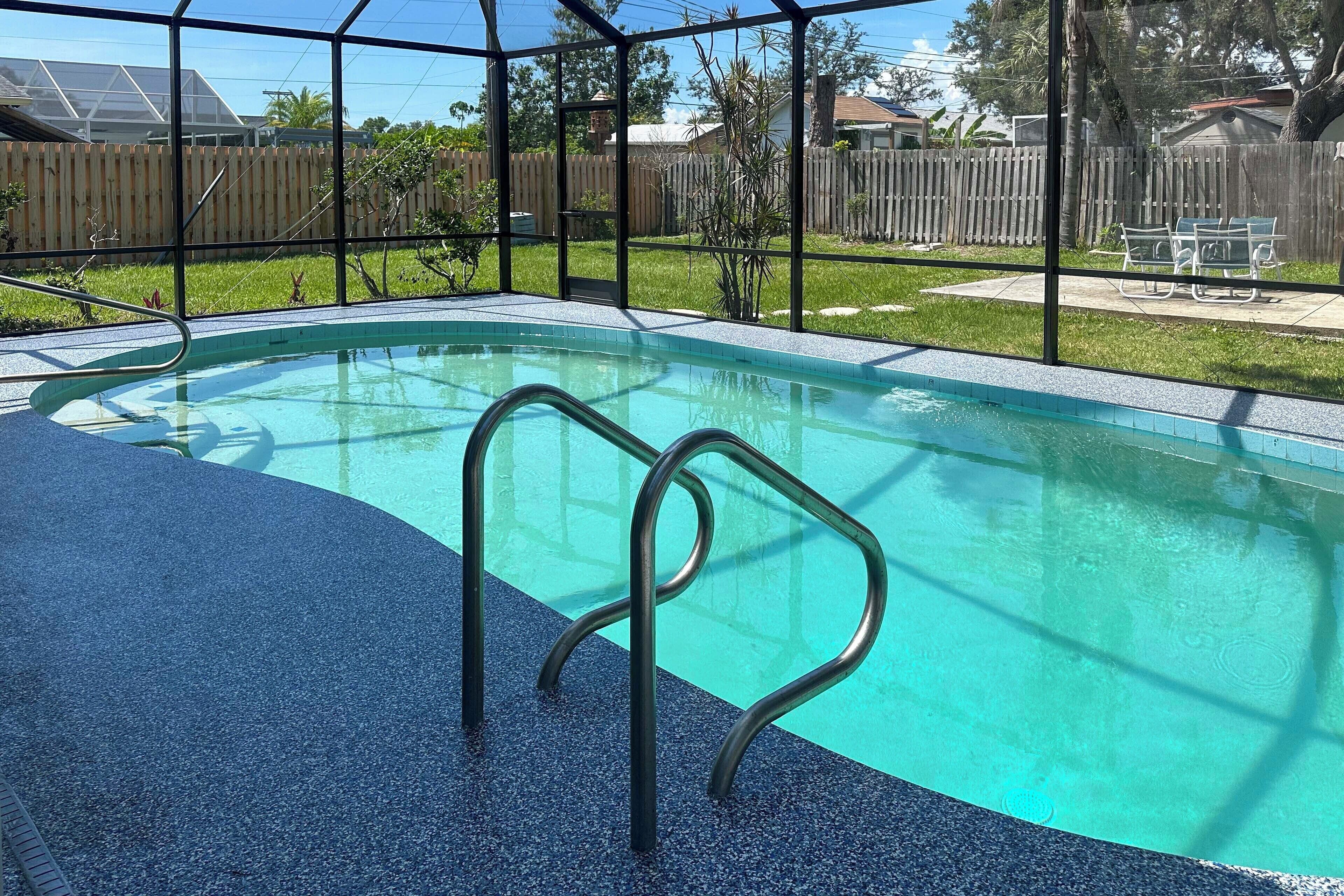 A swimming pool with a metal ladder, surrounded by a fence and a grassy area.