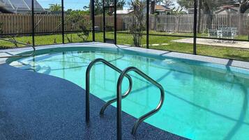 A swimming pool with a metal ladder, surrounded by a fence and a grassy area.