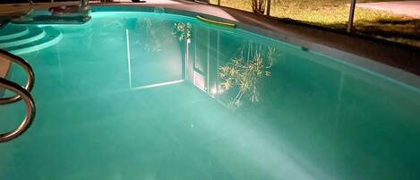 A swimming pool with clear water, a diving board, and a view of the surrounding area.