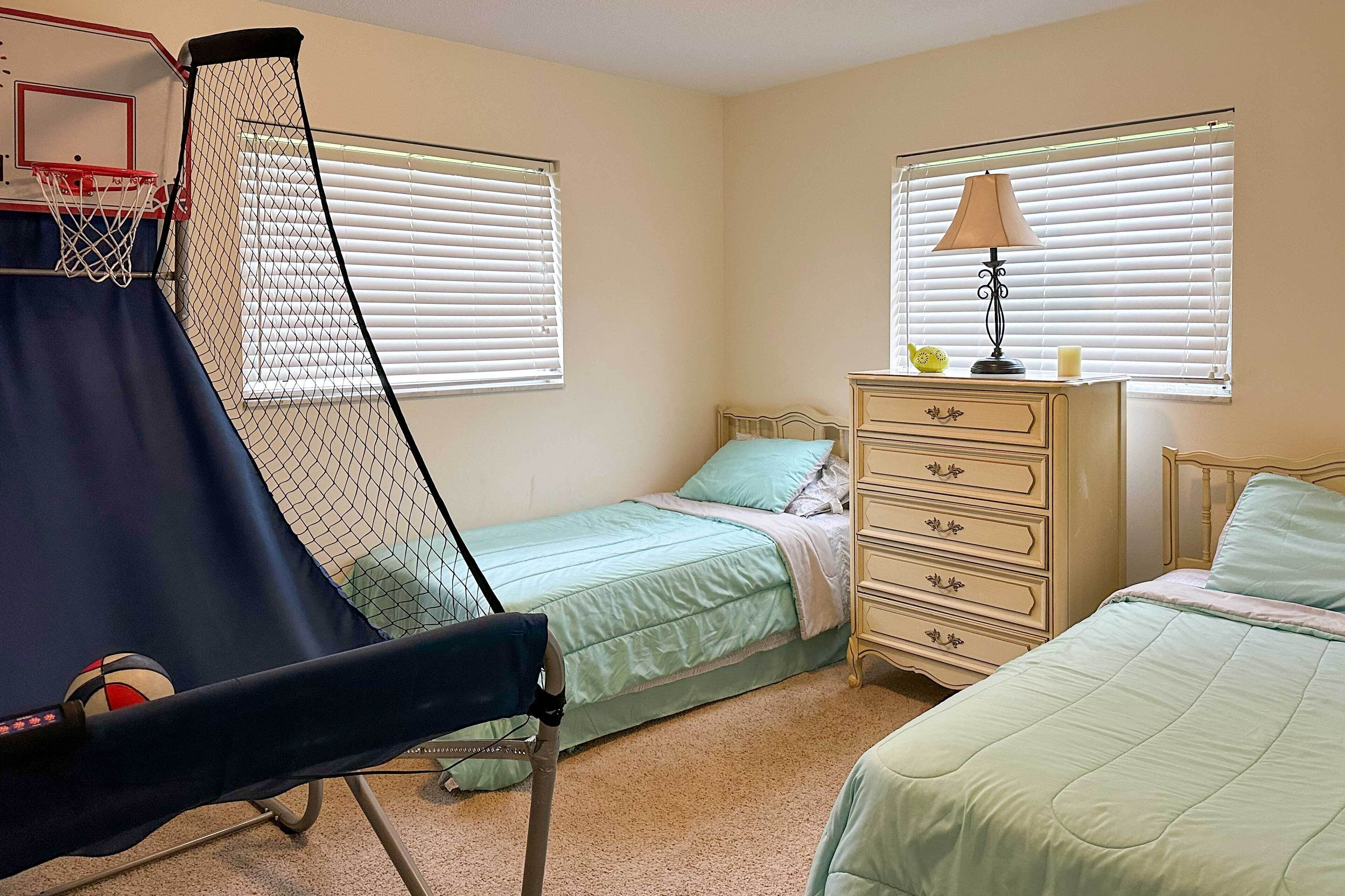 A bedroom with a bed, dresser, lamp, and a basketball hoop.