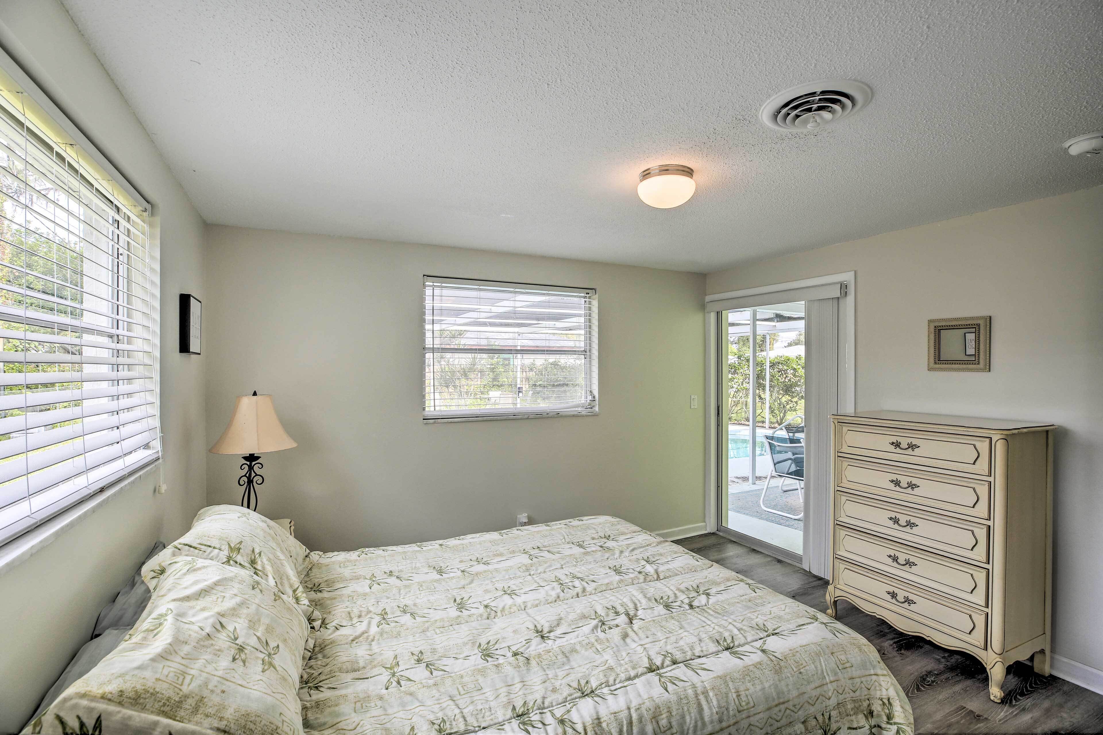 A bedroom with a bed, a dresser, a window with blinds, a ceiling light, and a door leading to a balcony.