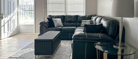 A modern living room with a leather sectional sofa, a glass coffee table, and a quilted rug.