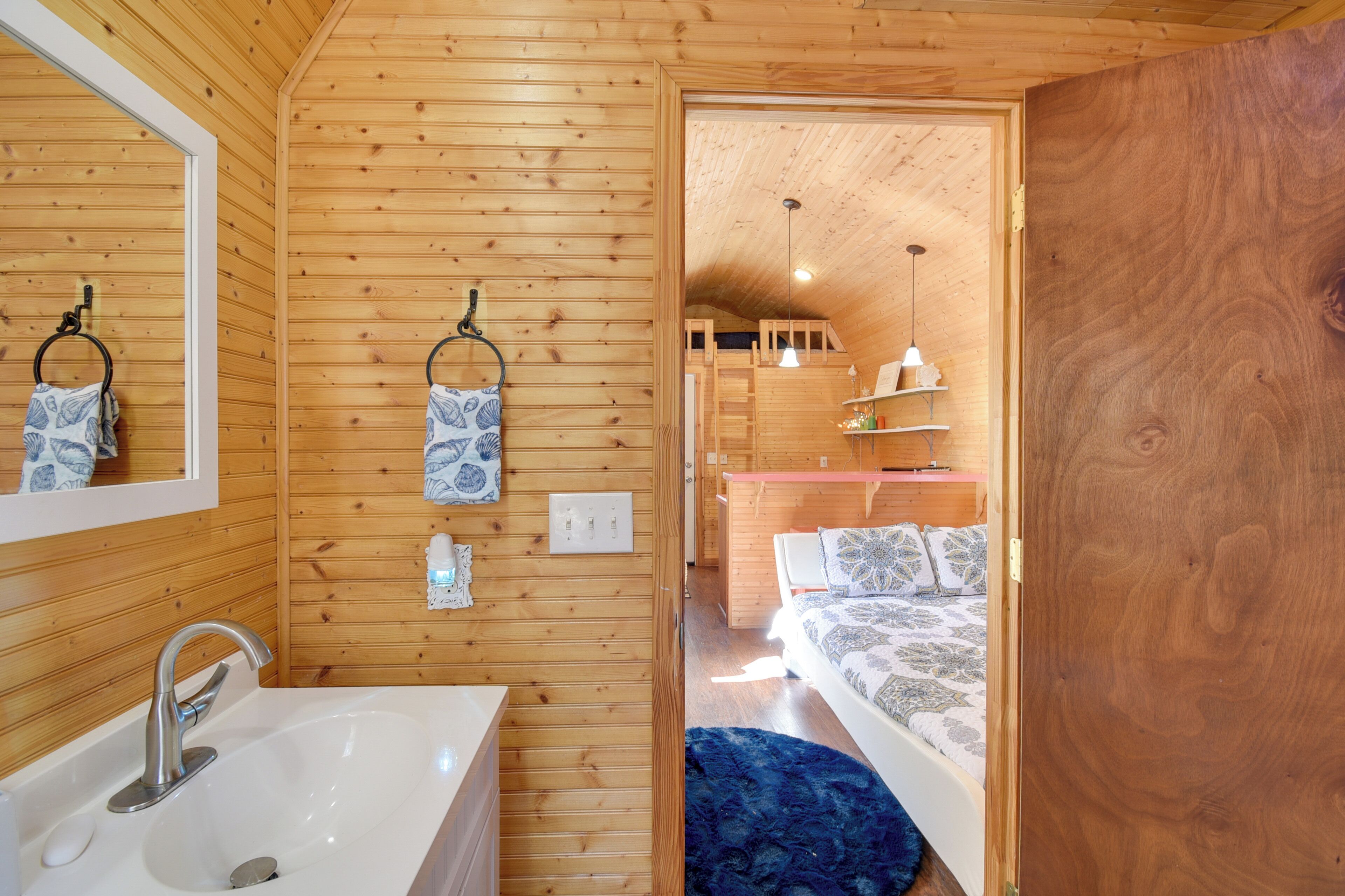 A wooden interior with a bathroom, a bed, and a small kitchenette.