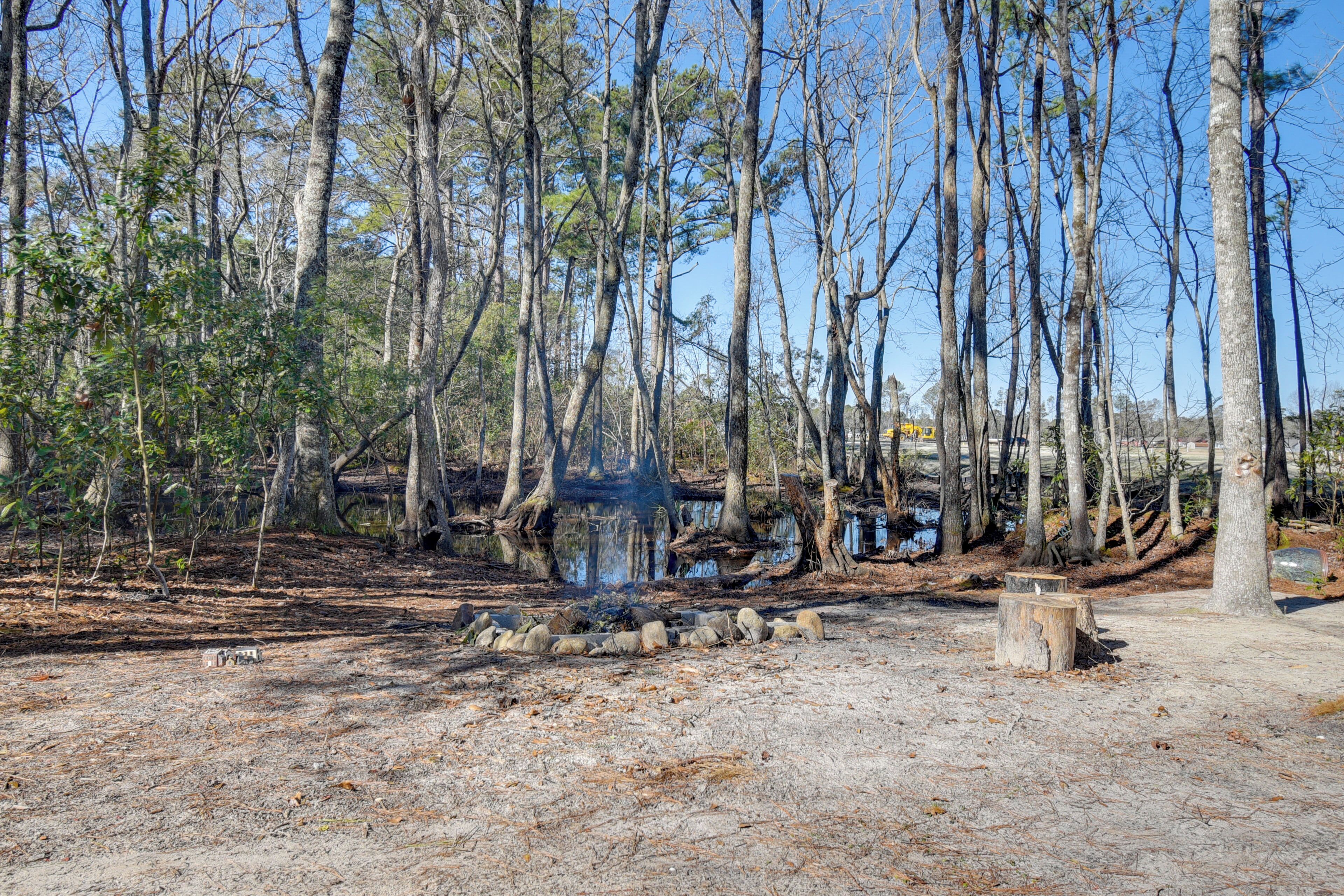 A campsite with a fire pit surrounded by rocks, trees, and a small body of water.