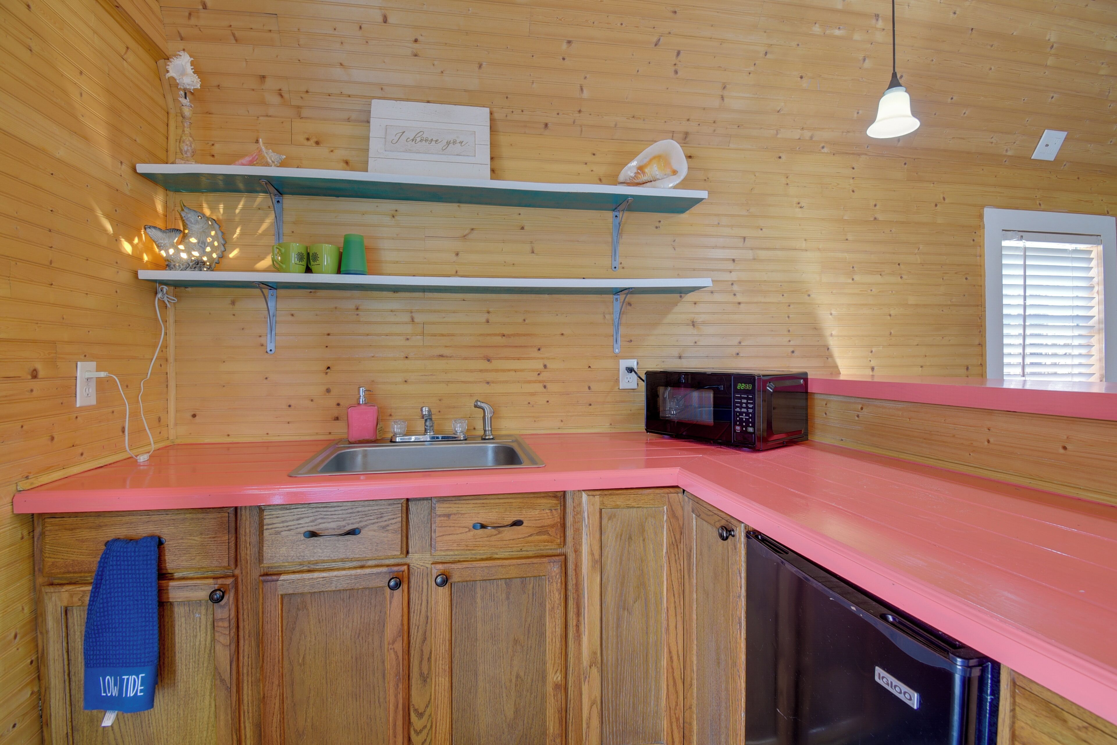 Een kleine keuken met houten kastjes, een roze aanrecht, een magnetron en een spoelbak.