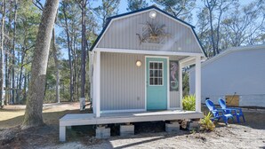 A small wooden cabin with a porch, a door, and two blue chairs outside. - Cozy Calabash Studio ~ 4 Mi to Sunset Beach! (Sunset Beach)