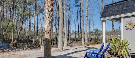 Une cabane en bois avec deux chaises bleues à l’extérieur, entourée de grands arbres et sous un ciel dégagé.