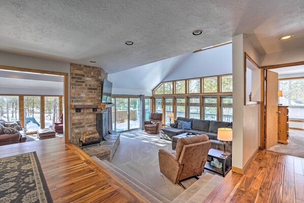 A spacious living room with a fireplace, large windows, and a high ceiling.