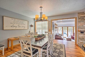 A dining area with a wooden table, white chairs, a chandelier, and a large framed quote on the wall.