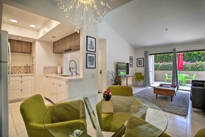 Una cocina moderna con armarios blancos, una zona de comedor con sillas verdes y una sala de estar con sofá y mesa de centro.