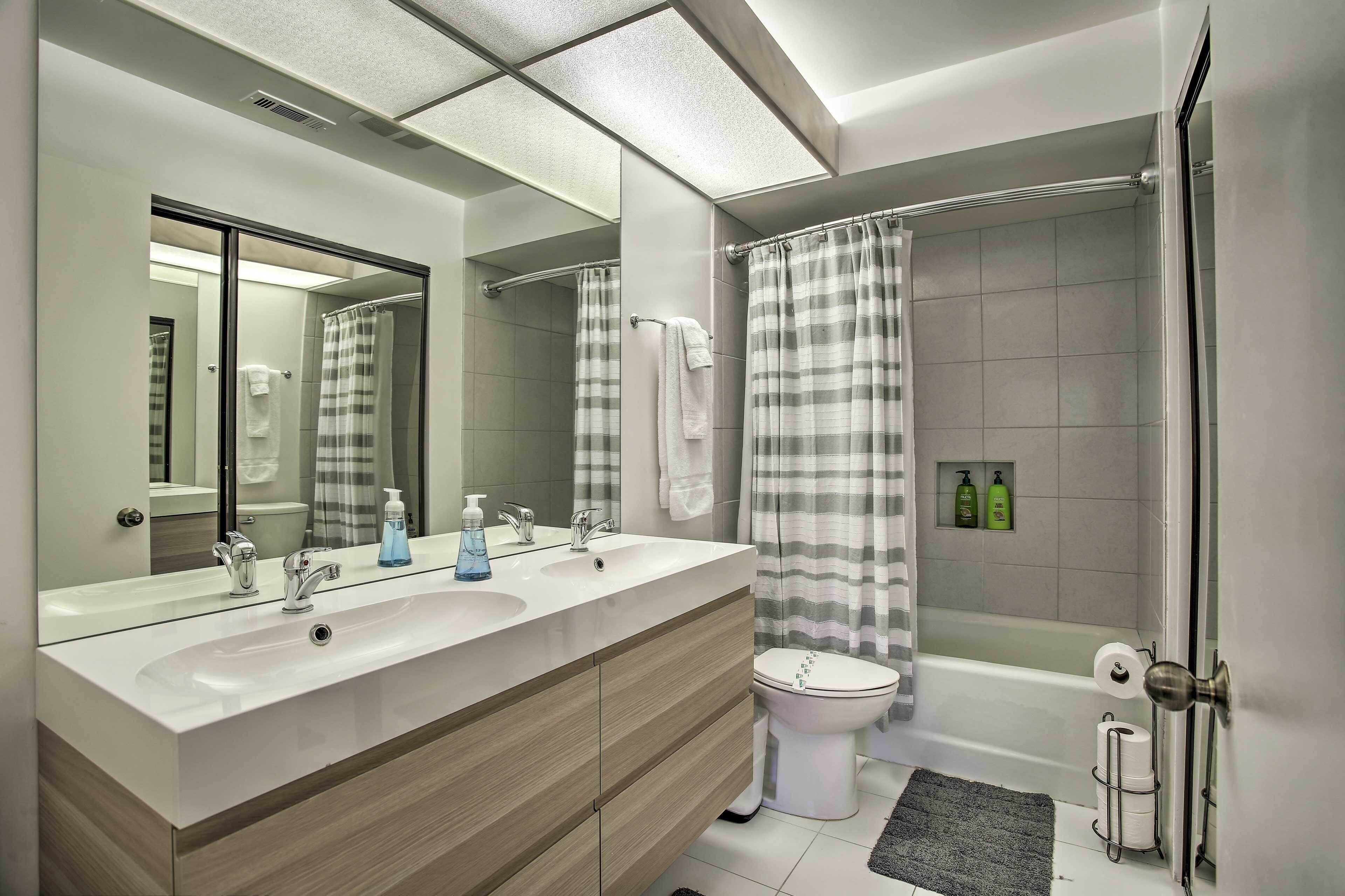 Ein modernes Badezimmer mit einem Doppeltiegel-Waschtisch, einer Toilette, einer Dusche mit gestreiftem Vorhang und einem Duschbereich mit Glasabtrennung.