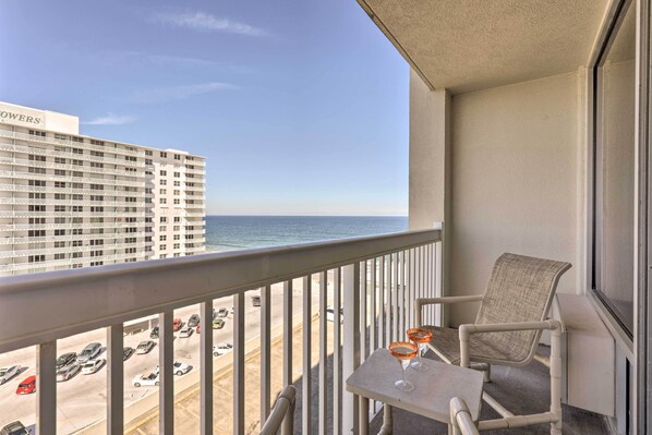 A balcony with a view of the ocean and a parking lot. There is a chair and a table with two drinks on it. - Ocean-view Daytona Beach Resort Retreat w/ Balcony (Daytona Beach)