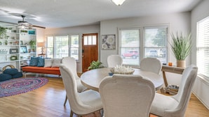 A dining area with a round table, white chairs, and a ceiling fan. There is a bookshelf with various items and a potted plant on the windowsill. - 1 Mi to Dtwn: Family-friendly Brenham Bungalow! (Brenham)