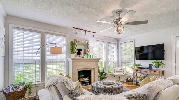 A living room with a fireplace, sofa, ottoman, and a ceiling fan. - 1 Mi to Dtwn: Family-friendly Brenham Bungalow! (Brenham)