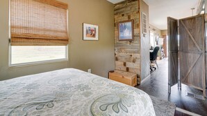 Ein Schlafzimmer mit einem Bett, einem Fenster mit Jalousien, einer Holzwand und einer Tür.