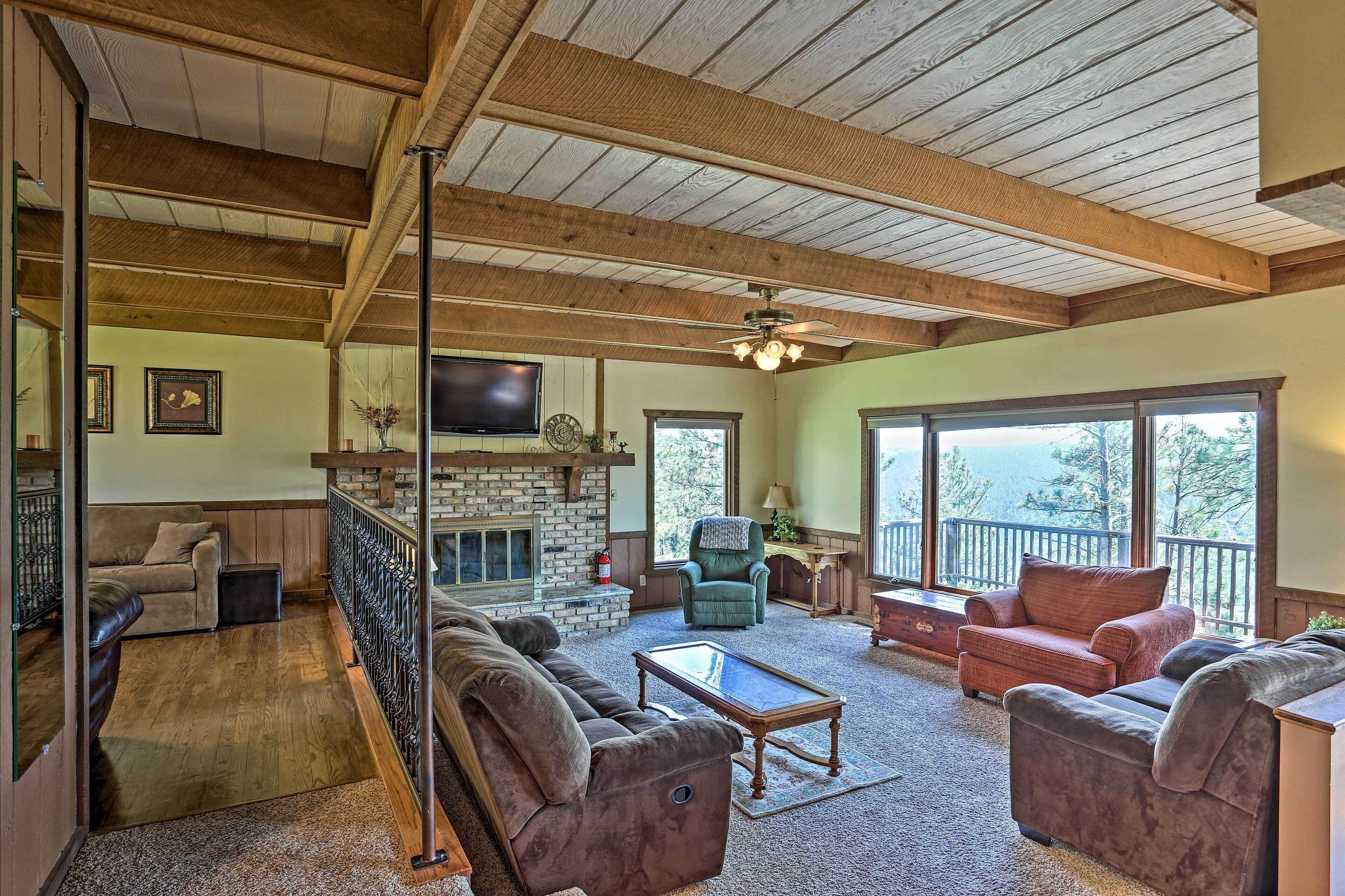 A spacious living room with a fireplace, comfortable seating, and large windows offering a view of the outdoors.