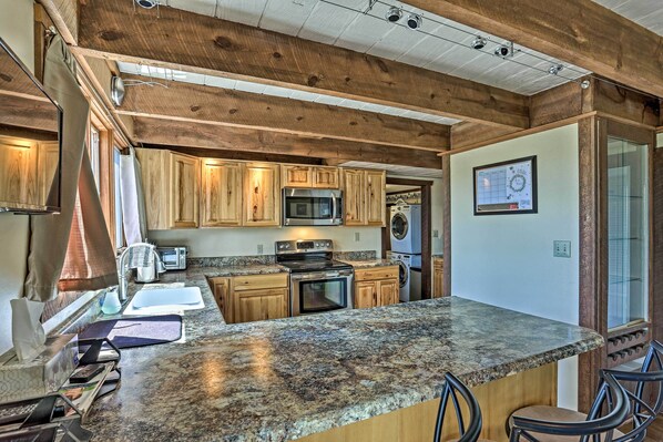 A kitchen with wooden cabinets, a granite countertop, stainless steel appliances, and a bar area with chairs.