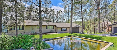A residential property with a swimming pool, surrounded by tall trees and a well-maintained lawn.