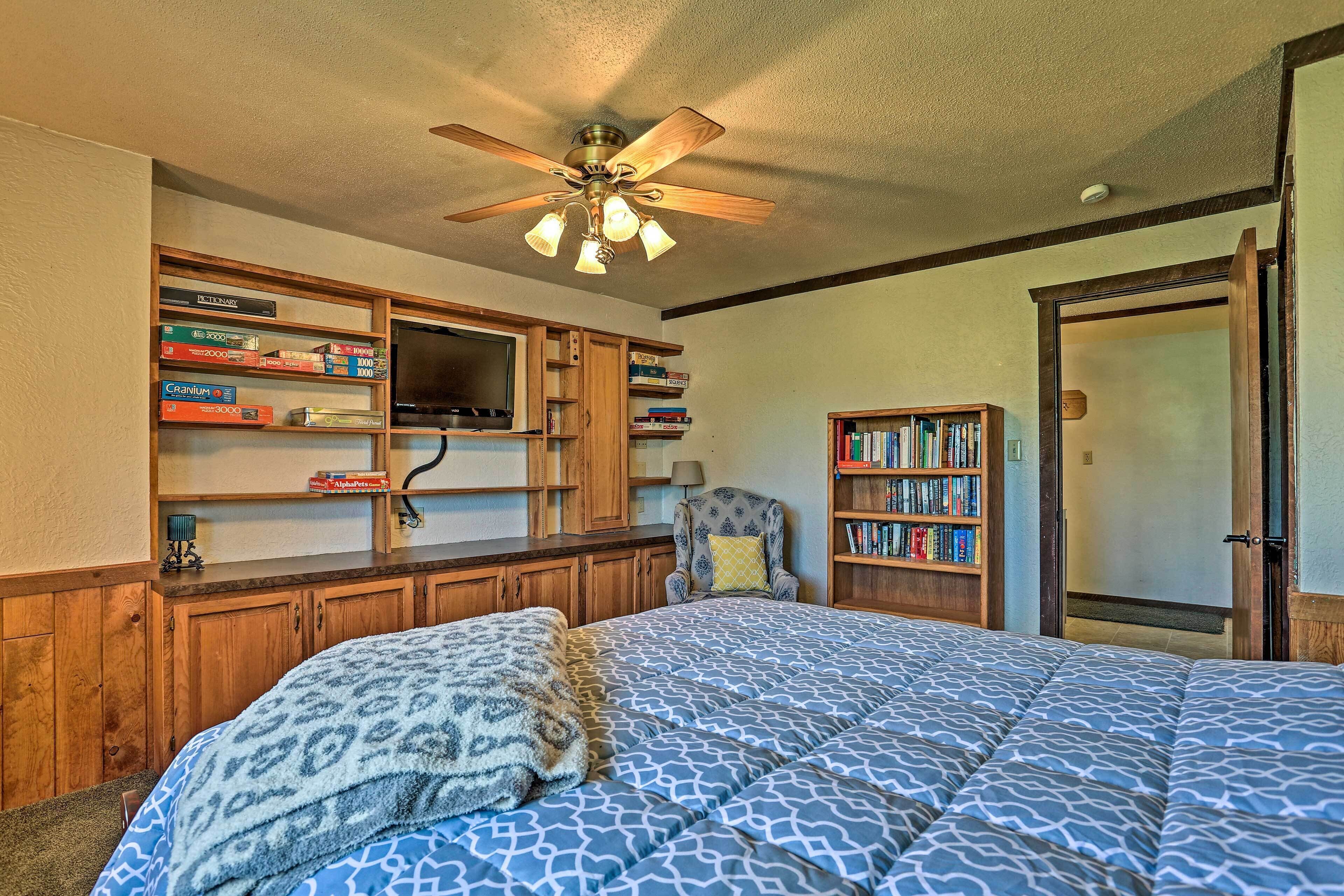 A bedroom with a bed, a ceiling fan, wooden cabinets, a bookshelf, and a door.