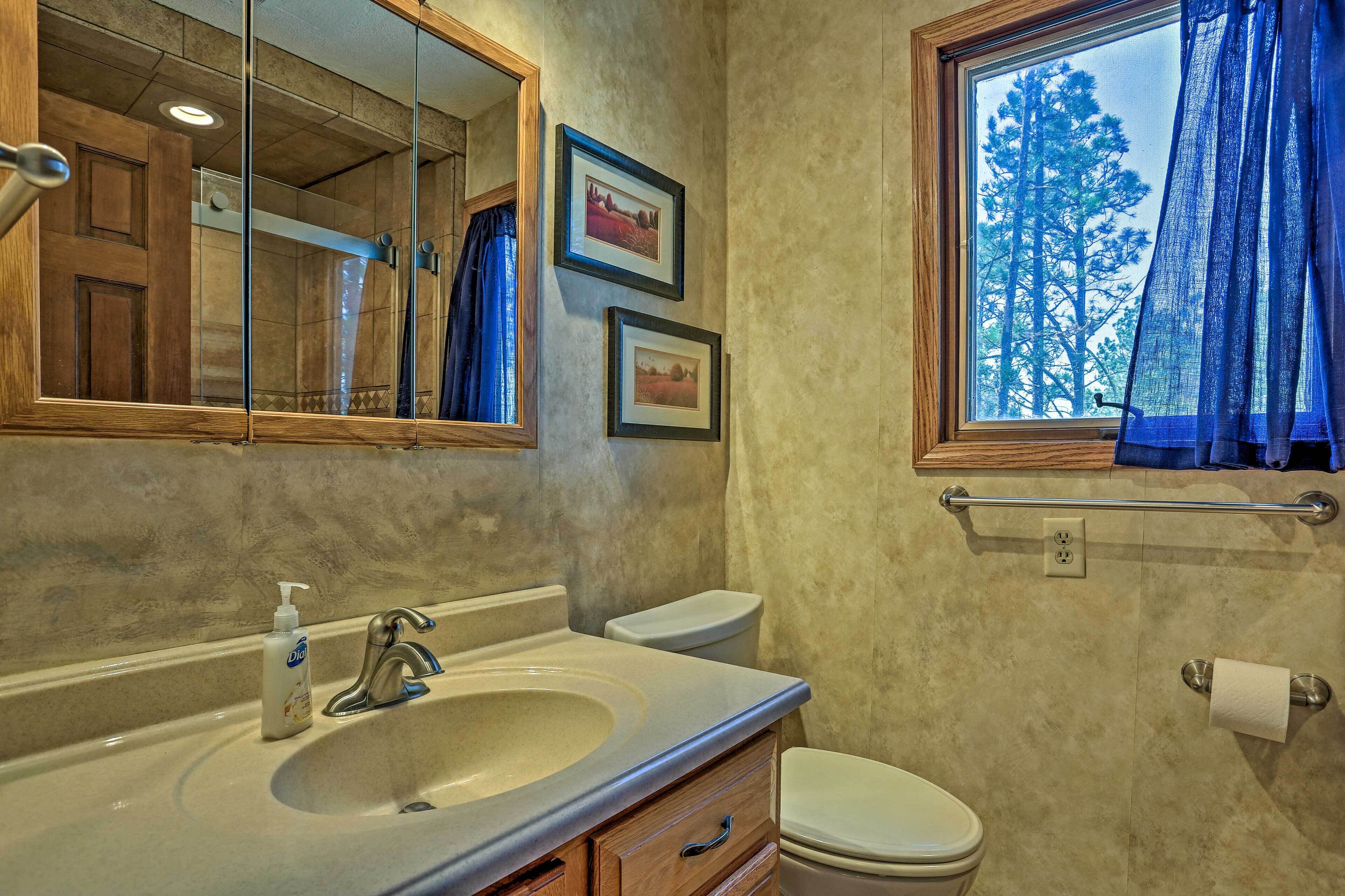 A bathroom with a sink, mirror, toilet, and window with curtains.