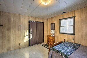A bedroom with wooden panel walls, a bed with a patterned bedspread, a dresser, a fan, and a window with blinds. - Secluded Irons Cabin w/ 5-acre Yard, Deck, Grill! (Irons)